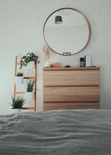 potted plant brown wooden 3-drawer chest with round brown wooden framed mirror in front of bed inside room plant